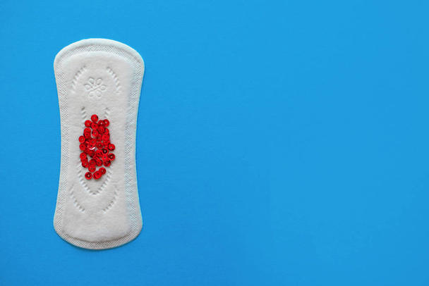 Menstrual pad with red sequins on a blue background, top view, miniature of the menstrual period - Fotó, kép