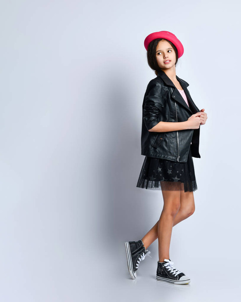 Teenage girl in black leather jacket, skirt, t-shirt, pink hat and sneakers. She posing standing isolated on white. Full length - Foto, imagen