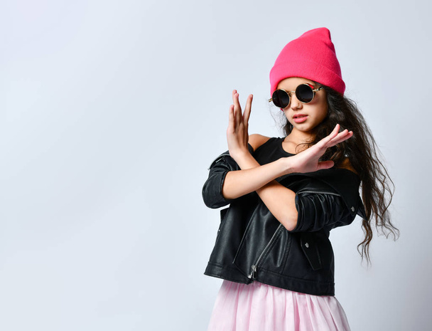 Teenage kid in black leather jacket, pink hat and sunglasses. Showing stop or no sign with gesture, isolated on white. Close up - Foto, Imagen