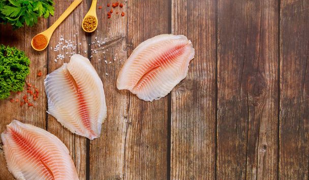 Raw tilapia fillets with seasonings over wooden background. - Photo, Image