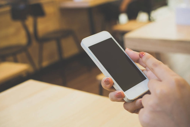 Рука крупным планом женщины с помощью смартфона на деревянном столе в ресторане, шаблон черного экрана устройства мобильного телефона
 - Фото, изображение