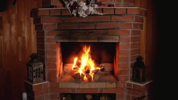 flame of fire burns in brick home Christmas fireplace. festive wreath hangs over fireplace. Wooden candlesticks is decorated with Christmas decor. Rest and relaxation in front of fireplace in evening. - Video, Çekim