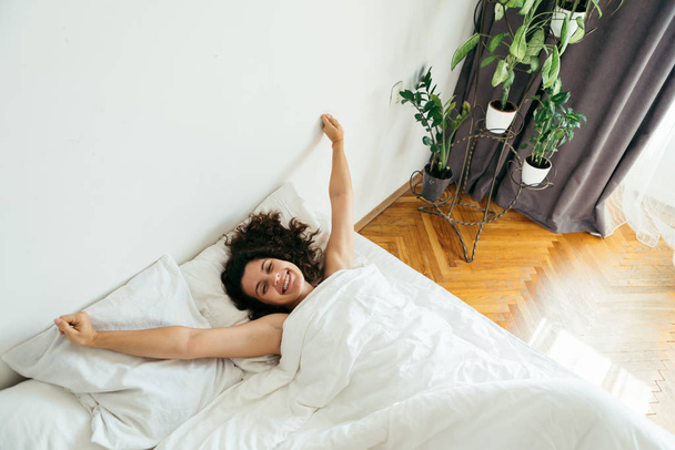 junge hübsche Frau im Bett mit weißen Laken helles Licht - Foto, Bild