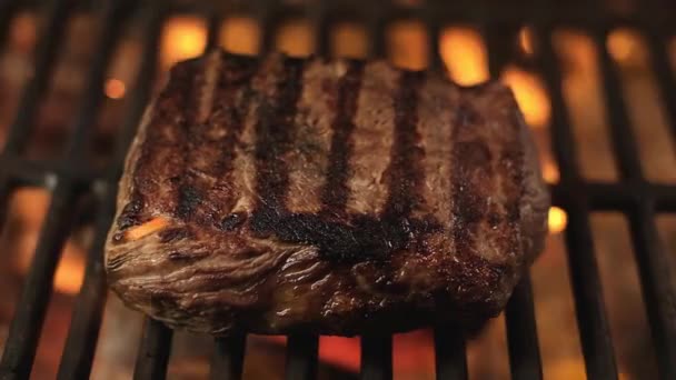 juicy piece of fried meat with beautiful stripes on hot grill on an open fire. Pork or beef cooked on grill in center of frame. Barbecue in nature. Meat fillet is fried on fire on a cast iron grill. - Footage, Video