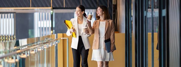 Banner, página web o plantilla de portada de dos mujeres de negocios asiáticas caminando y hablando durante el descanso de café en la oficina moderna o espacio de coworking, relajarse y hablar, concepto de asociación de negocios y personas
 - Foto, imagen