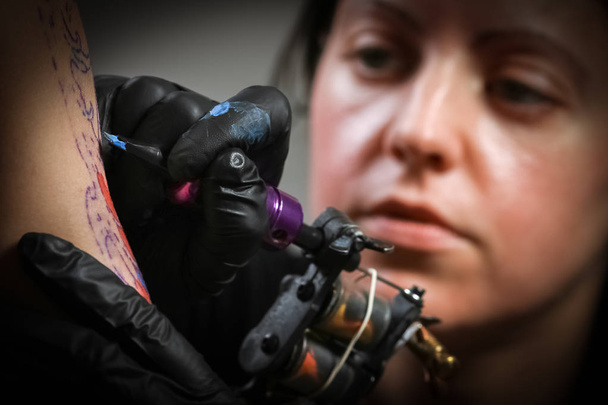 Bir adamın kolunda Dövme yapma kadın dövme sanatçısı - Fotoğraf, Görsel