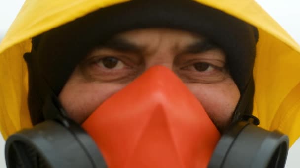 Retrato de um ecologista especialista em um respirador vermelho e um manto amarelo com um capuz. O inspetor olha atentamente para a câmera e remove lentamente sua máscara
. - Filmagem, Vídeo