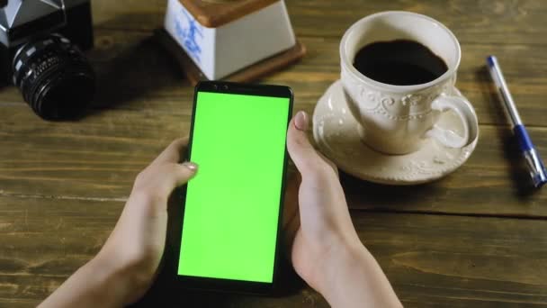 Девушка сидит дома за столом, держа смартфон с зеленым экраном. Жест подростка имитирует прокрутку фотографий на экране пальцем. Подходит для просмотра в Интернете или фотографий. Chromakey
 - Кадры, видео