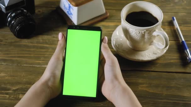 дівчина сидить вдома за дерев'яним столом і тримає смартфон з зеленим екраном. Цей жест імітує натискання кнопки на екрані пальцем. Використовується для перегляду в Інтернеті або для додатків. Хромакі - Кадри, відео