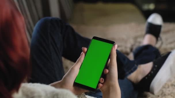mulher em jeans está descansando em casa no sofá e segurando smartphone. mockup verde
. - Filmagem, Vídeo