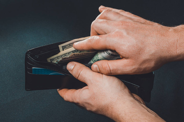 homem removendo dólares de sua carteira, mãos e carteira no fundo preto
. - Foto, Imagem