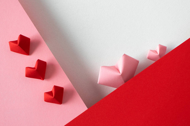 Roze en rode origami hartjes op witte achtergrond en papieren rand - Foto, afbeelding