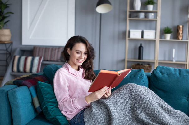Happy young woman relaxing reading sit on sofa at home.  - Valokuva, kuva
