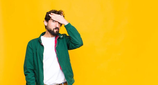 young crazy bearded man panicking over a forgotten deadline, feeling stressed, having to cover up a mess or mistake against flat wall - Fotoğraf, Görsel