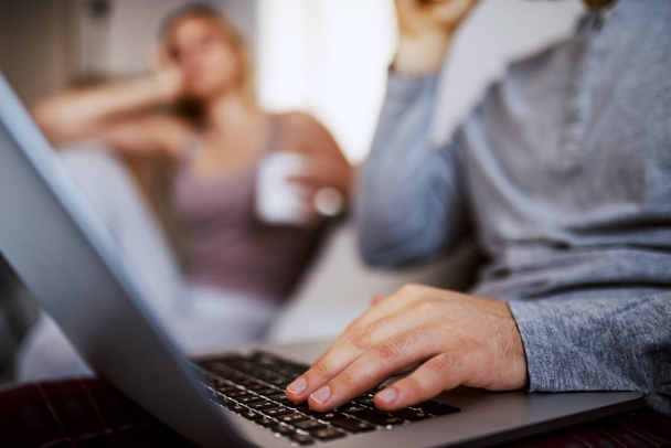 Крупним планом молодий чоловік використовує ноутбук для інтернет-серфінгу. Жінка в фоновому режимі сидить і стає нудно, тому що її хлопець ігнорує її
. - Фото, зображення