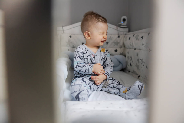 Adorable blond toddler sitting in his crib and sneezing. - Fotografie, Obrázek