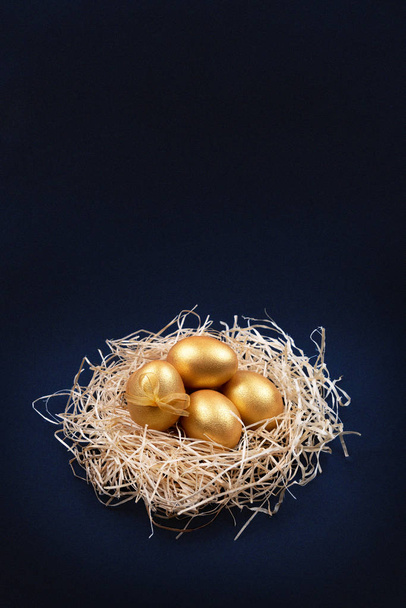 Золотисті кольорові великодні яйця в декоративному гнізді на темно-синьому фоні. Копіювати простір
. - Фото, зображення