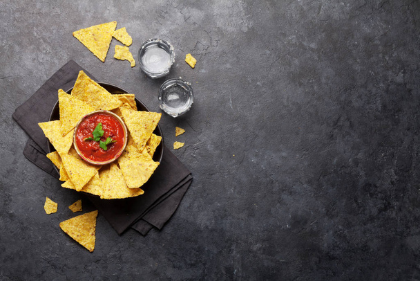 Nachos mexicanos fritos con salsa. Vista superior plana puesta en la mesa de piedra con dos tiros de tequila y espacio de copia
 - Foto, imagen
