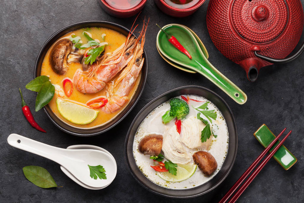 Tom Yum e Tom Kha tradicionais sopas tailandesas com frutos do mar, frango, cogumelos, leite de coco e especiarias quentes. Com panela de chá verde e tigela. Vista superior
 - Foto, Imagem