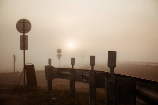 Sunrise and fog on the track, in the distance you can see the headlights of a passing car - 写真・画像