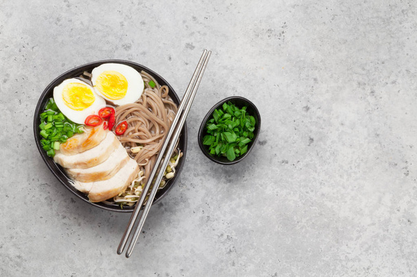 Asian noodle ramen soup with chicken, vegetables and eggs on stone background. Top view flat lay with copy space - Photo, Image