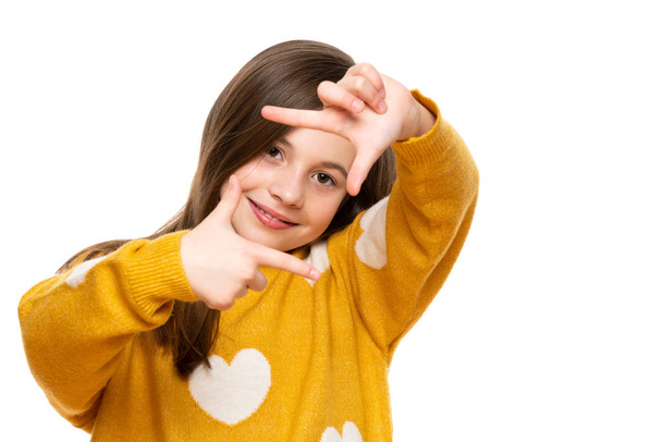 Adorable elementary age girl smiling while looking at camera and making photo frame hand gesture. Studio shot on white background. - Photo, Image