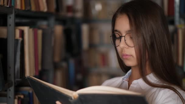 Portret van een jong meisje dat een boek leest in een bibliotheek - Video