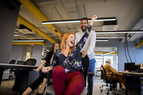 Young cheerful business people in smart casual wear having fun while racing on office chairs and smiling - Photo, Image