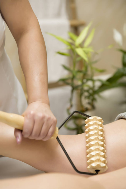Closeup of the maderotherapy anti-cellulite leg massage with wooden roller massager - Photo, Image