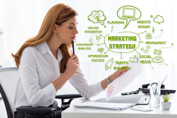 Vista laterale della donna d'affari in possesso di carta con grafici vicino a documenti e laptop sul tavolo, illustrazione della strategia di marketing
 - Foto, immagini