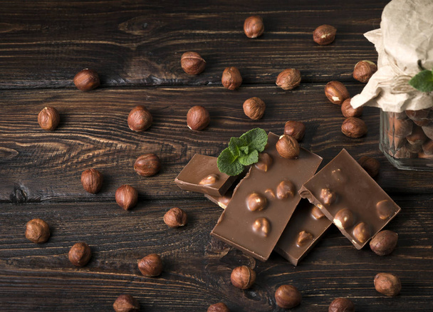Glas mit Haselnüssen und Schokolade mit Nüssen auf einem hölzernen Hintergrund - Foto, Bild