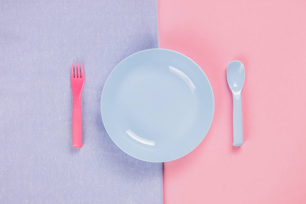 Blue plastic plate with spoon and fork on pink background - 写真・画像