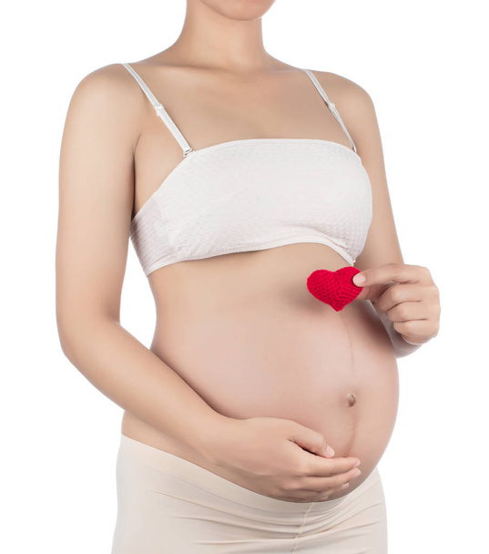 Έγκυες γυναίκες και το χέρι κρατήσει ένα κόκκινο σύμβολο της καρδιάς τοποθετείται στην κοιλιά  - Φωτογραφία, εικόνα