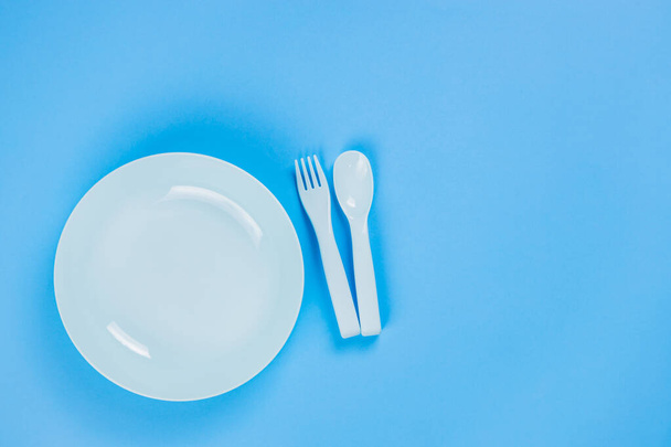 Blue plastic plate with spoon and fork on blue background - Fotó, kép