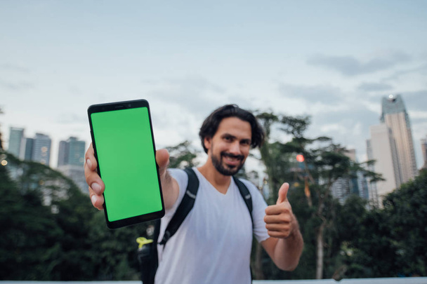 A man holds a phone with a green screen and stands against the b - Photo, image