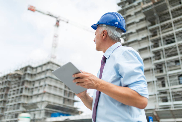 Architect using his tablet in front of a big construction site - Photo, Image