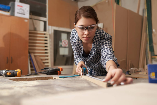 Young woman woodworker with wooden board behind workbench - Photo, Image