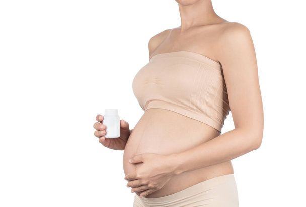 Живіт вагітної жінки і таблетки в руці ізольовані на білому
  - Фото, зображення