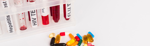 panoramiczne ujęcie probówek z próbkami krwi i literami w pobliżu tabletek odizolowanych na biało  - Zdjęcie, obraz
