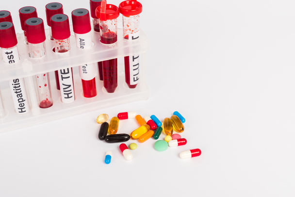 δοκιμαστικούς σωλήνες με δείγματα αίματος και γράμματα κοντά σε χάπια που απομονώνονται σε λευκό  - Φωτογραφία, εικόνα