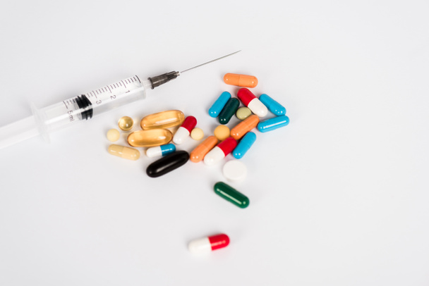 pílulas coloridas perto da seringa no branco com espaço de cópia
  - Foto, Imagem