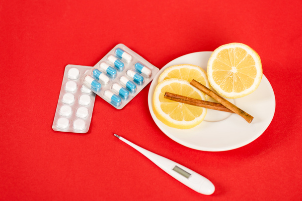 limones en rodajas en platillo con palitos de canela cerca de pastillas y termómetro digital en rojo
  - Foto, Imagen