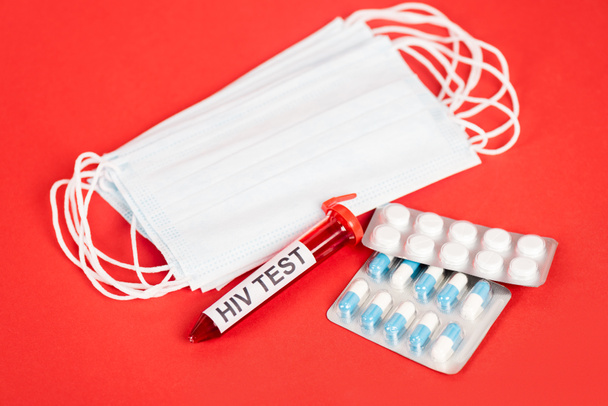 muestra con letras de prueba de VIH cerca de pastillas y máscaras médicas en rojo
  - Foto, Imagen