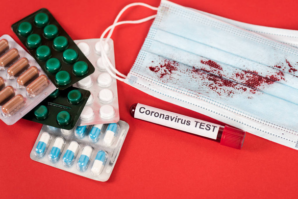 monster met coronavirus test belettering in de buurt van pillen en medisch masker met bloed op rood  - Foto, afbeelding