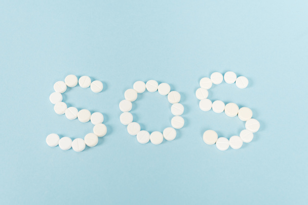top view of pills with sos lettering on blue  - Fotoğraf, Görsel