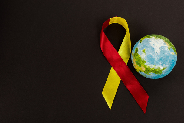 vista superior del globo cerca de la cinta roja y amarilla como la hepatitis c conciencia aislada en negro
  - Foto, imagen