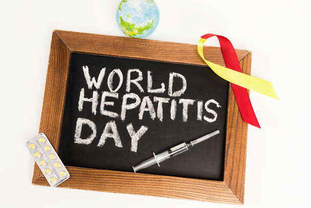 Kreidetafel mit Welt-Hepatitis-Tag-Schriftzug in der Nähe von Band, Globus, Pillen und Spritze isoliert auf weiß  - Foto, Bild