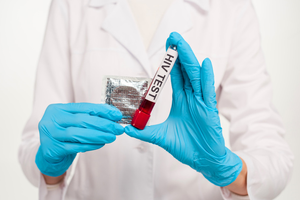 vista recortada del científico en guantes de látex sosteniendo la muestra con letras de prueba de VIH y preservativo aislado en blanco
  - Foto, imagen