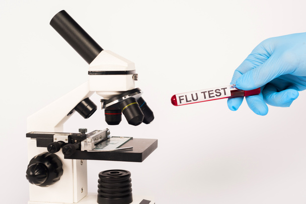 visão recortada do cientista em tubo de teste de retenção de luva de látex com letras de teste de gripe perto do microscópio isolado em branco
  - Foto, Imagem
