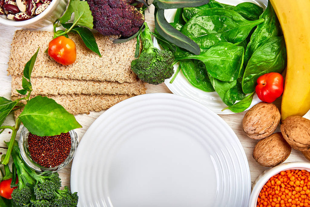 Επιλογή τροφίμων πλούσια σε φυτικές ίνες σε λευκό ξύλινο φόντο γύρω από άδειο πιάτο, Υγιή διατροφή των τροφίμων προϊόν. Πάνω άποψη, επίπεδη lay, αντίγραφο χώρου - Φωτογραφία, εικόνα